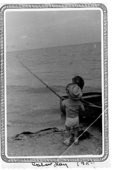 A b/w photo of a toddler fishing from the shore from the 1950s.