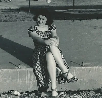 Carol's mother sitting outside with her legs crossed and hands on her knees.
